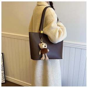 Detail of dark brown leather tote bag with gold hardware and plush bear charm accessory