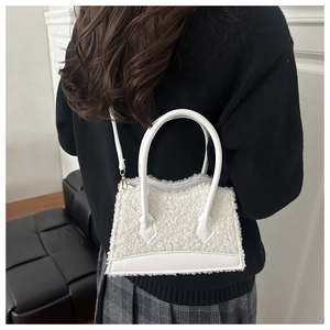 Detail of white faux fur handbag with smooth leather strap worn over a black sweater