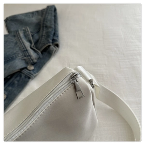 Detail of the high-quality silver metal zipper and white fabric texture on a trendy crossbody bag