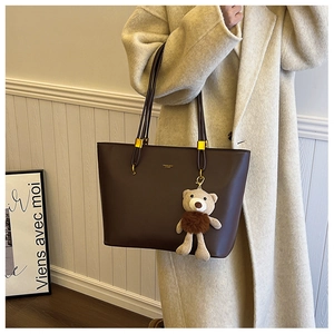 Detail of a large dark brown faux leather tote bag with cute bear charm worn by a model