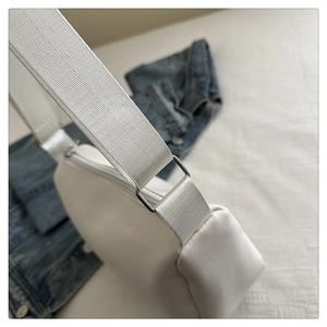Close-up of white crossbody bag showing wide fabric strap and silver square metal buckle