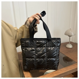 Makroaufnahme einer schwarzen gesteppten Nylon-Puffertasche mit Glanzfinish und Tragegriffen