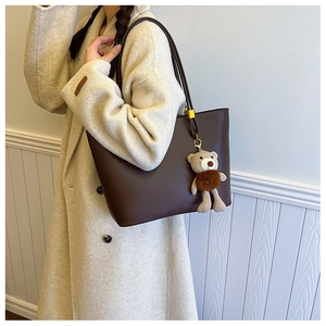 Detail of a large brown leather tote bag with a cute plush bear charm on its strap