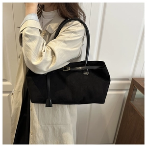 Detail view of a black matte leather tote bag featuring a gold buckle and slim straps