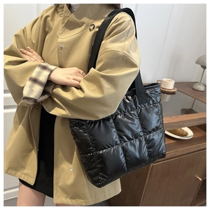 Detailed view of black quilted puffer tote bag worn by a model in a cozy indoor setting