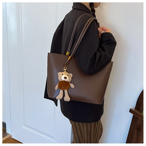 Close-up of a large brown tote bag with a plush bear charm and golden hardware