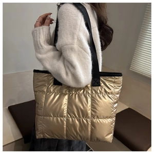 Close-up of golden quilted tote bag with metallic finish and wide black shoulder straps