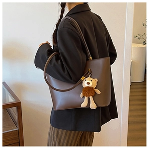 Deep brown PU leather tote bag with a cute teddy bear charm on a female shoulder