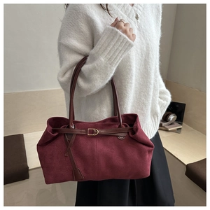 Detail of burgundy suede tote bag featuring brown leather straps and gold buckle accents