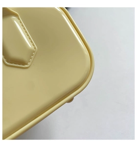 Close-up of cream yellow glossy patent leather bag showing precise stitching and metallic feet