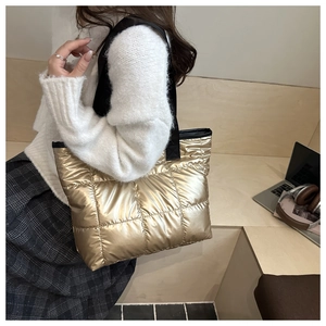 Close-up of golden quilted tote bag with black canvas strap in a cozy indoor setting