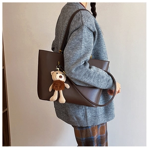 Detail of dark brown faux leather tote bag with a cute beige teddy bear pendant charm