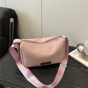 Pink nylon crossbody bag with wide strap and fashion patch on black wood table
