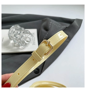 Close-up of cream yellow patent leather belt with a square gold metal buckle and hand