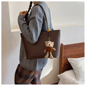 Detail showing plush bear charm on minimalist dark brown PU leather tote bag with matte finish