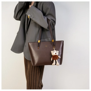 Detail of dark brown tote bag with gold logo, metal hardware and bear charm