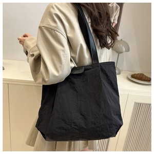 Detail of black pleated nylon tote bag with fashion logo label carried on shoulder