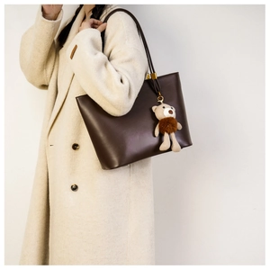 Large brown leather tote bag on beige coat with a cute plush bear charm detail