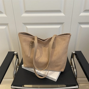 Large beige suede tote bag with leather handles displayed on a black chair for commuting