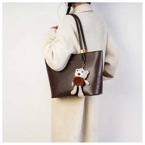 Detail of dark brown leather tote bag with a cute knit bear charm on white wool coat