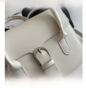 Macro shot of silver metal buckle and stitching details on cream leather crossbody bag