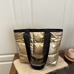 Quilted gold metallic tote bag with black nylon straps on a cozy beige knit background