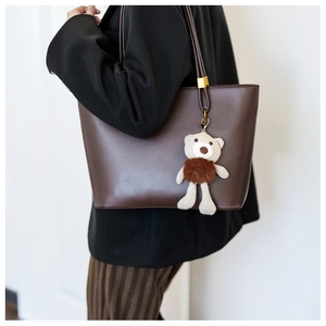 Detail of deep brown faux leather tote bag with a cute teddy bear charm on the strap