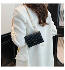 Detail of black quilted crossbody bag with gold chain strap and letter logo on white blazer