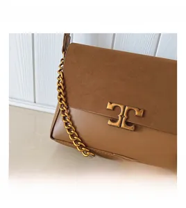 Detail of brown suede and leather crossbody bag with gold chain and metal emblem