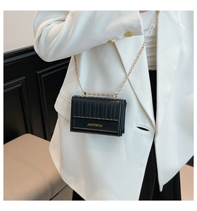 Detail of black mini crossbody bag with vertical quilting and elegant gold chain strap