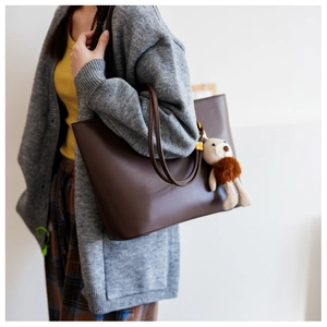 Detail of large brown leather tote bag featuring a cute knit bear pendant accessory