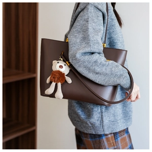 Detail of vintage brown PU leather tote bag with a cute knit bear pendant on shoulder strap