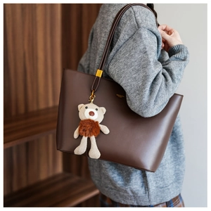 Close-up of brown leather tote bag with cute bear charm worn by a model