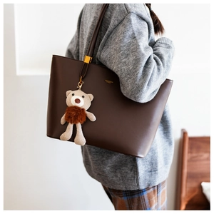 Close-up of brown PU tote bag featuring a cute plush bear charm and matte leather texture