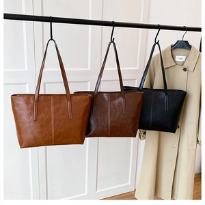 Detailed view of leather tote bags in light brown, dark brown, and black hanging on a rack