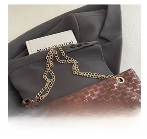 Close-up of golden chain strap and monogrammed texture on brown tote bag