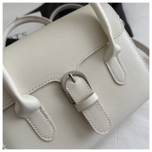 Macro detail of silver metal buckle and premium stitching on white leather handbag