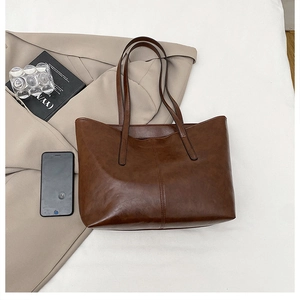 Flat lay of vintage dark brown tote bag with leather texture beside a beige blazer