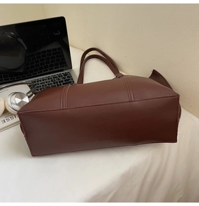 Détail du sac cabas marron foncé avec ordinateur et casque sur un bureau de travail