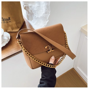 Detailed view of brown suede and leather shoulder bag with gold metal logo and chain strap