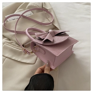 Detail einer rosafarbenen Handtasche mit Strass-Schleife auf einem beigen Blazer