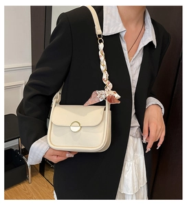 Detail of cream crossbody bag featuring a golden buckle and floral scarf on strap