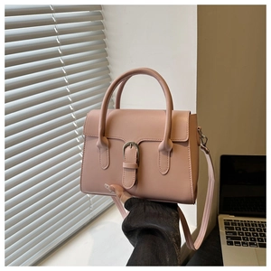Detail of a dusty pink crossbody handbag featuring a polished metal buckle and top handle