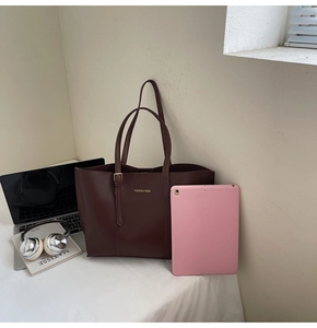 Détails d'un grand sac cabas bordeaux avec lettrage doré sur un bureau épuré