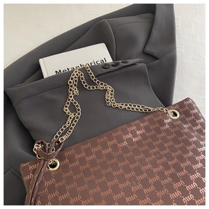 Detail of dark brown tote bag with letter pattern and double golden chain straps