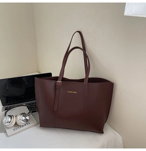 Détail d'un sac cabas en cuir bordeaux avec lettrage doré sur un bureau minimaliste