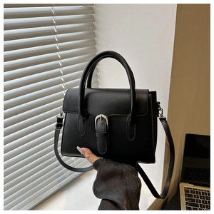 Detail of matte black leather handbag with silver buckle on minimalist workplace background