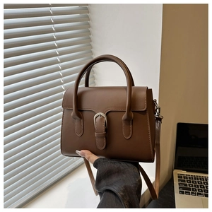 Close-up of dark brown matte leather handbag with horseshoe metal buckle and adjustable strap