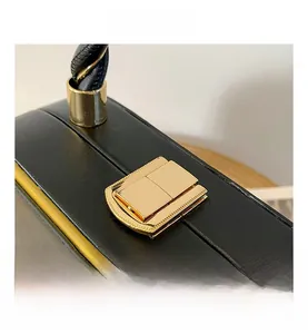 Detail of golden metal press buckle on black litchi pattern leather handbag with woven handle
