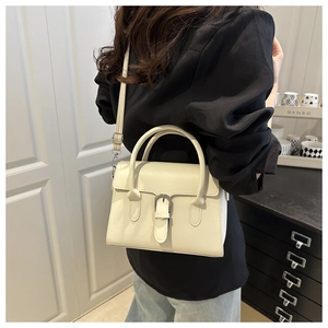 Detail of cream faux leather handbag featuring metal buckle and adjustable shoulder strap